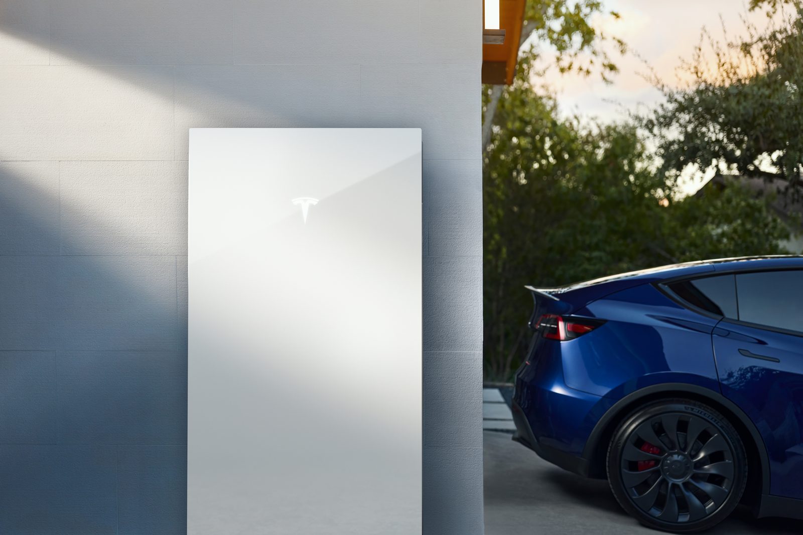 Tesla Powerwall installed on a home exterior wall with a Tesla Model Y parked beside it